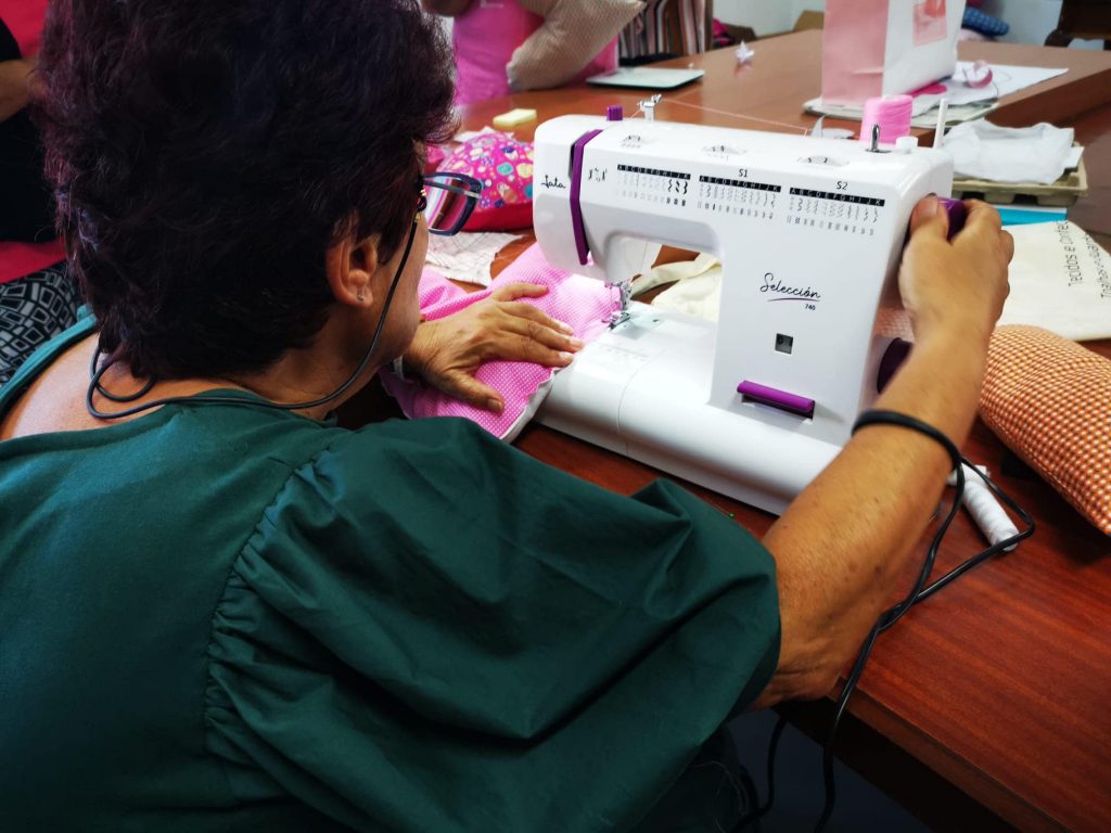 Vista posterior de uma senhora que costura almofads de coração numa máquina de costura.
