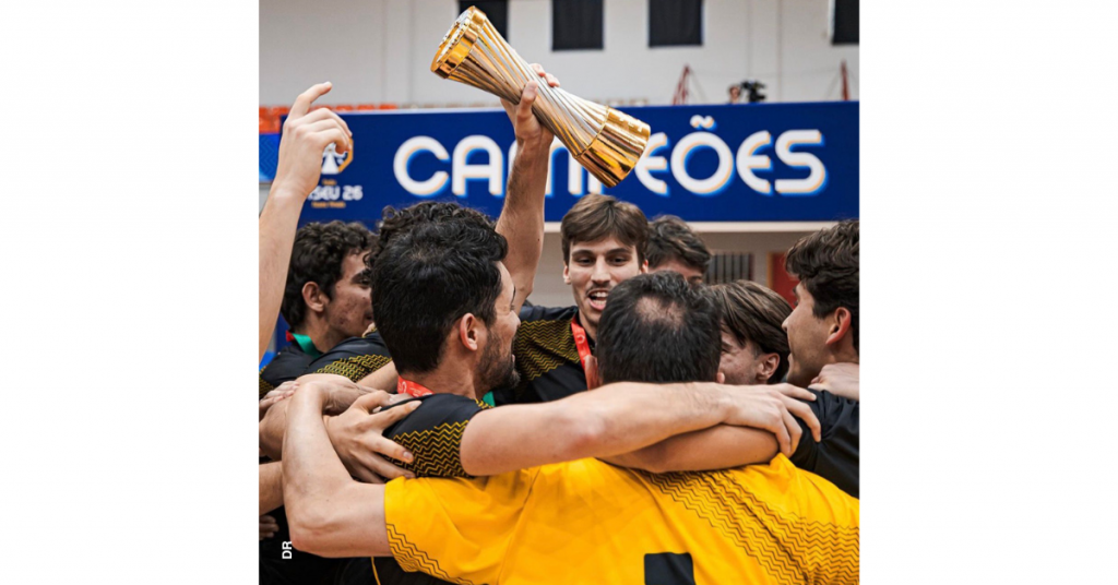 Equipa masculina de futsal do Instituto Politécnico de Leiria festeja a conquista do título de campeão nacional. O grupo de jovens está abraçado. Um deles, ao centro, ergue na mão a taça, doirada. Atrás, numa faixa a azul, lê-se, em letras brancas: "Campeões".