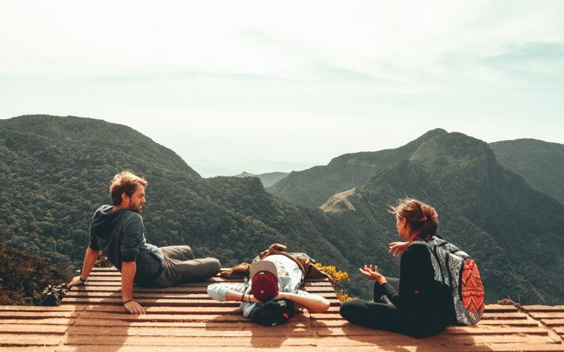 Três jovens sentados num miradouro com vista para montanhas