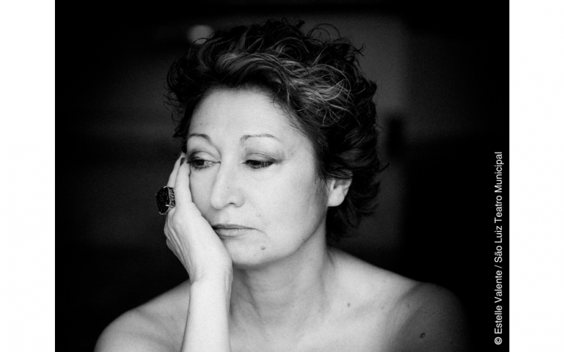 A bailarina e coreógrafa Olga Roriz aparece representada numa fotografia a preto e branco, dos ombros para cima. A sua mão direita apoia a cara e os seus olhos estão baixos, a apontar para a sua direita e para baixo.